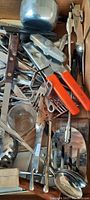 Assorted vintage kitchen utensils including can openers with orange Bakelite handles, metal spatulas, forks, scoops and ladles