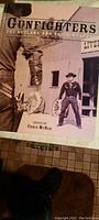 Cover of the vintage book titled 'Gunfighters: The Outlaws and Their Weapons' edited by Chris McNab showing a sepia-toned image of cowboy gunfighters in front of a Western storefront.