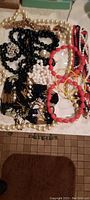 Overview of vintage costume jewelry laid out on a surface, showing heavy long red necklace alongside multiple pearl, black, white beaded necklaces and bracelets