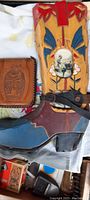 Wooden boot art display piece painted with red, blue, yellow, and brown colors, photo windows containing vintage photos, intact spur attached at the heel, and part of an embossed leather wallet visible on the side.