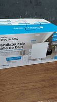 Photo of the DewStop Breeze Easy bathroom fan box showing front with product branding and key features.
