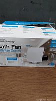 Photo of DewStop Breeze Easy Bath Fan box showing product name, features, and branding.