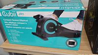 Cubii JR1 elliptical exercise device box showing a person using the device with feet in pedals. Black and teal colors with digital display on the front.
