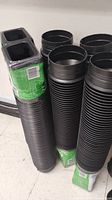 Four black ribbed downspout extension pipes stacked together inside a building.