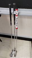 Three clubs standing together, two with black grips and one with white/red SuperStroke grip