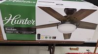 Front of packaging showing Hunter brand, Brenham model, five-blade fan with light