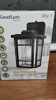 Front view of boxed Good Earth outdoor LED wall lantern, showing product image, brand, and key features.