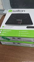 Two boxed Salton slim induction cooktop hot plates stacked showing brand and model on box front and side.