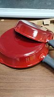 Two red enameled cast iron skillets stacked, showing red glossy exterior and black handles.