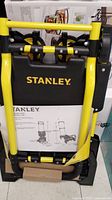 Front view of folded cart showing yellow steel frame, black plastic components and Stanley logo