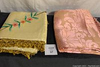 Two folded queen size bedspreads, one yellow with fringe, one pink with damask pattern