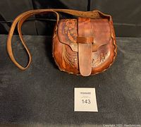 Front view of a brown 1970s floral tooled leather shoulder bag with scalloped edges and a wide strap.