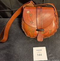Front view of vintage brown tooled leather shoulder bag with floral design and wooden bead closure.