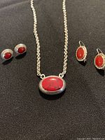 Front view of 925 silver necklace with large oval red stone and two pairs of red stone silver earrings on black fabric.