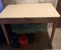 Full view of antique enamel top table, showing cream enamel surface and painted brown base with drawer.