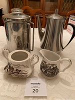 Front view of all four items: stovetop coffee percolator, stainless steel coffee server, ceramic creamer, ceramic sugar bowl with scenic brown pattern.