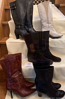 Photo showing six pairs of women's boots: two brown leather Nine West boots with buckles, a pair of black leather tall boots, cream colored tall 1980's boots, black wide calf boots, and dark brown suede boots.