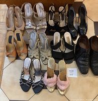 Twelve pairs of women's shoes and one pair of men's dress shoes arranged on floor including heels, sandals and slippers in various colors and styles