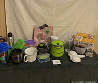 Photo showing all lot contents arranged on black surface including Crock-Pot Lunch Crock, lunch containers, drinkware, and bag