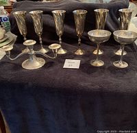 Five tall silver champagne flutes, two champagne coupes, and a two-arm candelabra arranged on a dark cloth.
