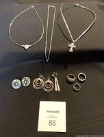 Full set of silver jewelry including three necklaces, three pairs of pierced earrings, and three rings arranged on black surface.