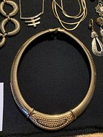 Close-up of a large gold-tone collar necklace with textured and detailed segments