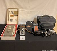 Full lot display showing boxed Polaroid Land Camera 150 with manuals, Kodak Brownie Target Six-20 box camera, four additional pocket cameras, and black Sakai camera bag.