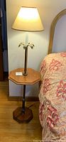 Full view of vintage floor lamp with attached wood table, lamp turned on, showing wood octagonal table surface and fabric shade.