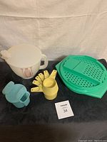 Overview of the four vintage Tupperware kitchen items on black background: white mixing bowl with lid, pastel blue sugar dispenser, harvest gold yellow measuring cups stack, jade green grater with container base.