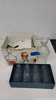 Box containing one glass decanter with stopper and four matching glasses in blue holder.