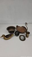 Photo shows six brass items including a swan-shaped planter, brass duck, bowl, small cup, apple-shaped container, and an oval mirror frame.
