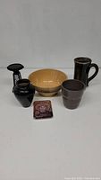 Photo of six ceramic decorative items including bowl, pitcher, vases, cup, and trivet.