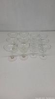 View of 16 clear glass champagne coupes arranged in two rows, showing hollow stems of two sizes.