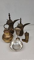 Two Middle Eastern drink pots, brass or bronze kettle, silverplate goblet and bowl, metallic boot figurine grouped on white surface