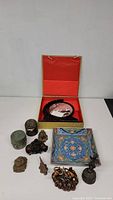 Overview of all Asian decorative items displayed including framed embroidery, ceramic containers, brass figurines, and decorative carved pieces.