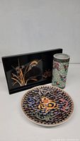 Photo showing three Asian decorative items: black lacquer tray, painted ceramic vase, decorative dragon plate.