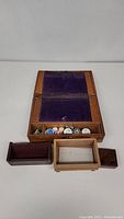 Fold out wooden writing desk opened showing purple felt interior with various wooden boxes and sewing supplies arranged below.