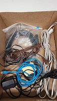 Box containing various cables and cords of different colors and types, some coiled and some loose