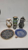 Group of six ceramics including three pitchers, two decorative plates, and a small Shakespeare figurine.