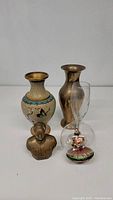 Photo showing cloisonné vase, bronze bust, metal vase, and glass ornament grouped together on a white background.