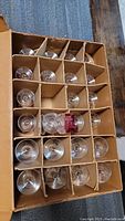 18 King's Crown thumbprint stemware glasses packed in a cardboard box with dividers. One glass has red flash decoration with damage visible.