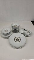 Photo showing stacks of plates, bowls, cups and saucers with Noritake decorative pattern in white, gold and dark accents.