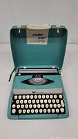 Front view of open teal Smith Corona typewriter showing keyboard and keys