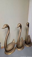 Front view of three brass swan sculptures side by side against wall