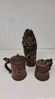 Photo showing two wooden tankards with lids and a detailed wood carving figure placed behind them