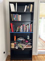 Front view of the Ikea bookcase filled with various books and small items, showing four shelves and the black finish.