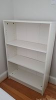 Front view of white bookcase showing three shelves and adjustable shelf holes on sides.