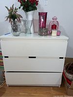 Front view of white wooden dresser with three drawers, some visible damage at the bottom ends.
