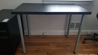 Front view of black rectangular table with silver metal legs on wood floor against a wall.