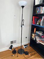 Full view of black floor lamp with white bowl shade and small reading light, standing next to bookshelf